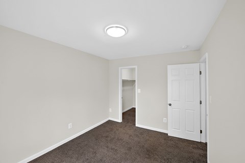 an empty bedroom with a white door and carpeted floor
